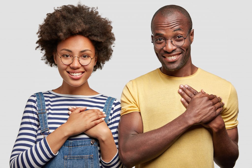 Imagem de uma mulher e um homem negros, lado a lado, com as mãos em formato de concha encostada no lado esquerdo do peito em alusão ao coração e como funciona um programa de fidelidade