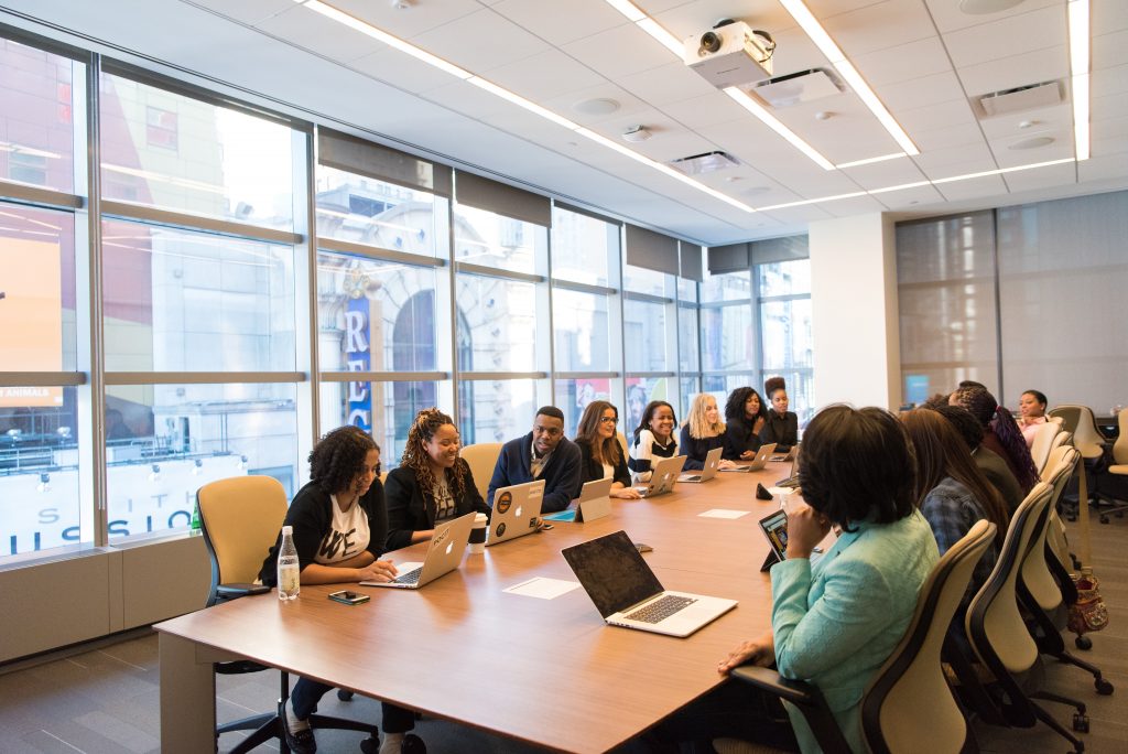 Imagem de uma sala de reuniões com mulheres sentadas à mesa, discutindo sobre algo